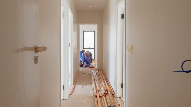 Renovatiebudget plannen tijdens woningrenovatie met nieuwe vloer en werkende vakmensen in smalle gang