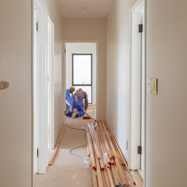 Renovatiebudget plannen tijdens woningrenovatie met nieuwe vloer en werkende vakmensen in smalle gang