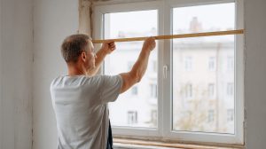 Man meet kozijnbreedte op met meetlint bij verbouwing woonkamer